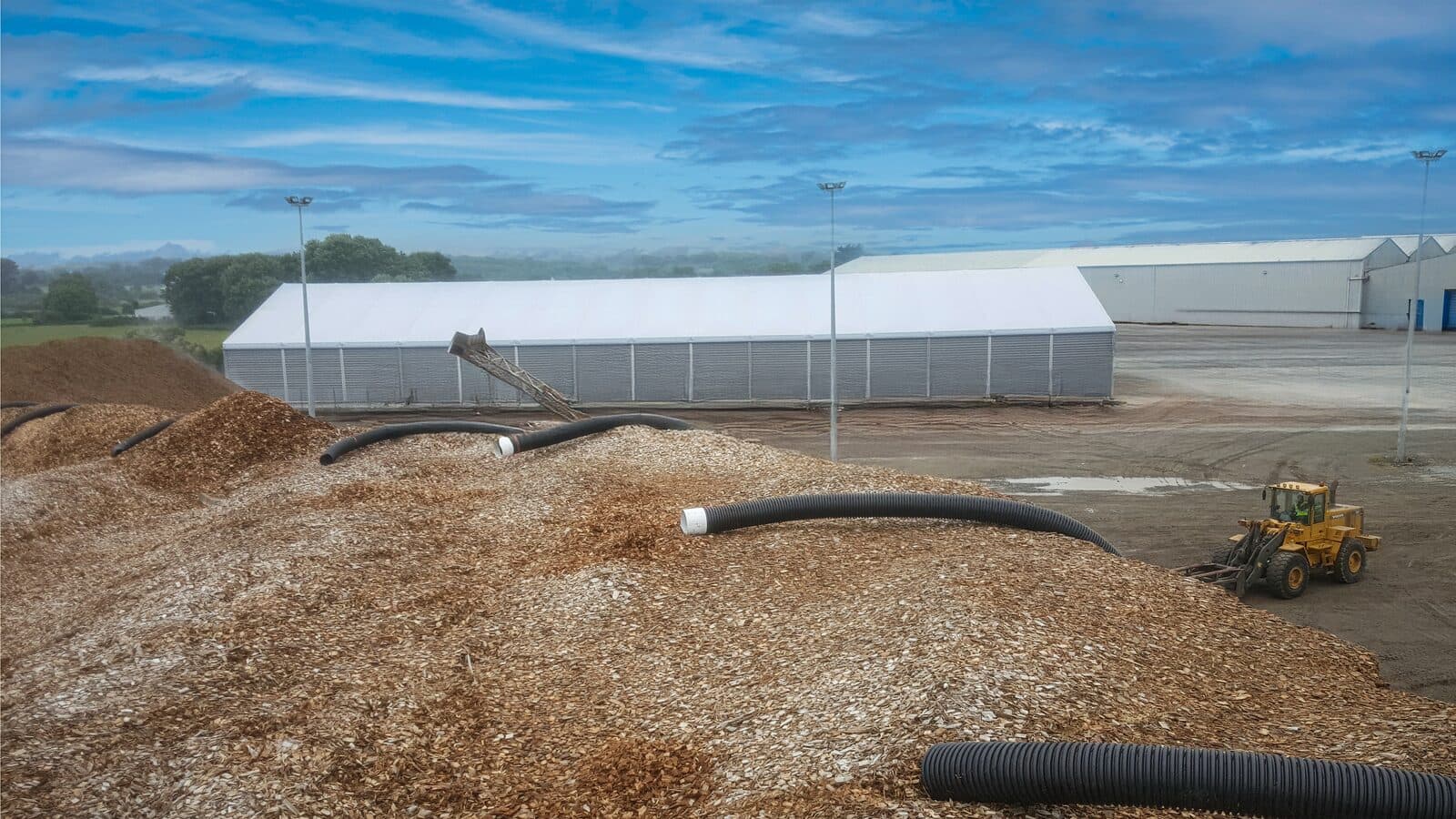 Woodchip stockpile aeration and loader operations at a port-side storage area.